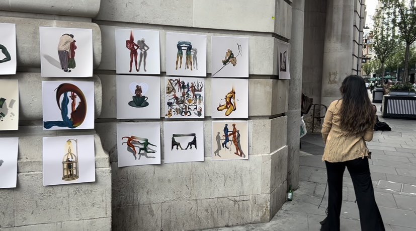 Passersby browsing artworks hung on a stone wall at an outdoor street show